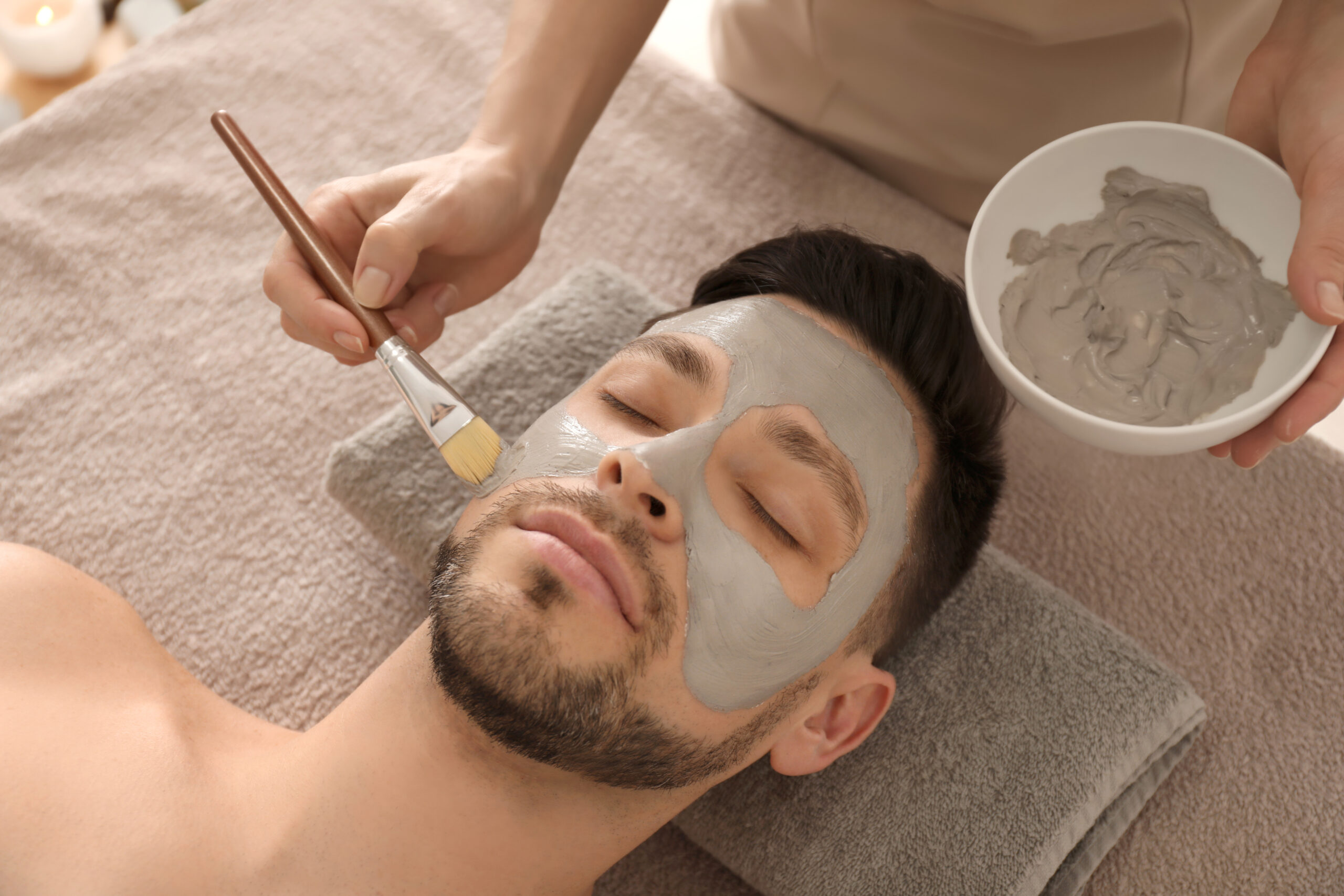 Cosmetologist applying cosmetic mask on man's face in spa salon